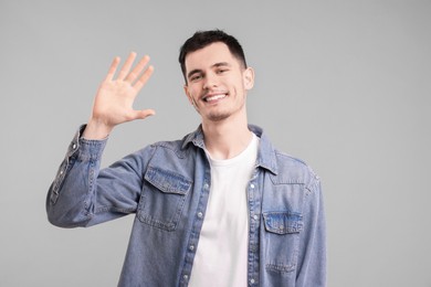 Photo of Happy young man waving on gray background