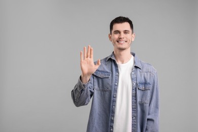 Happy young man waving on gray background, space for text