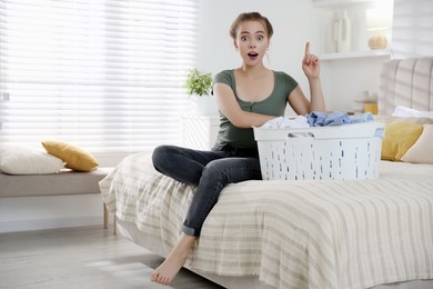 Photo of Emotional housewife with basket full of laundry on bed at home