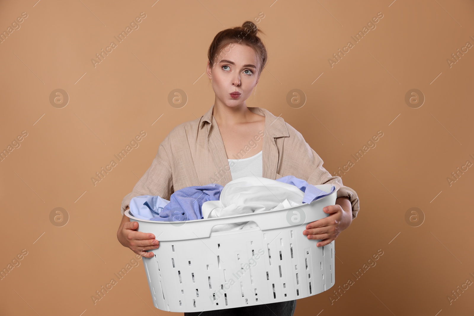 Photo of Young housewife with basket full of laundry on pale orange background