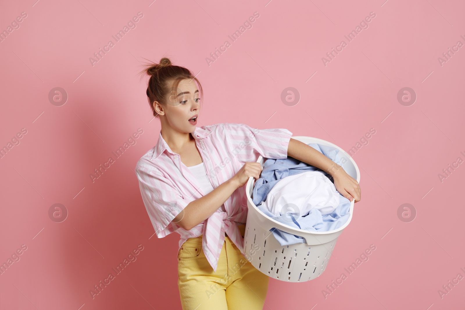 Photo of Emotional housewife with basket full of laundry on pale pink background