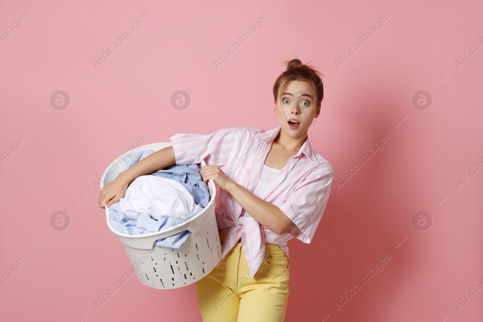 Photo of Emotional housewife with basket full of laundry on pale pink background