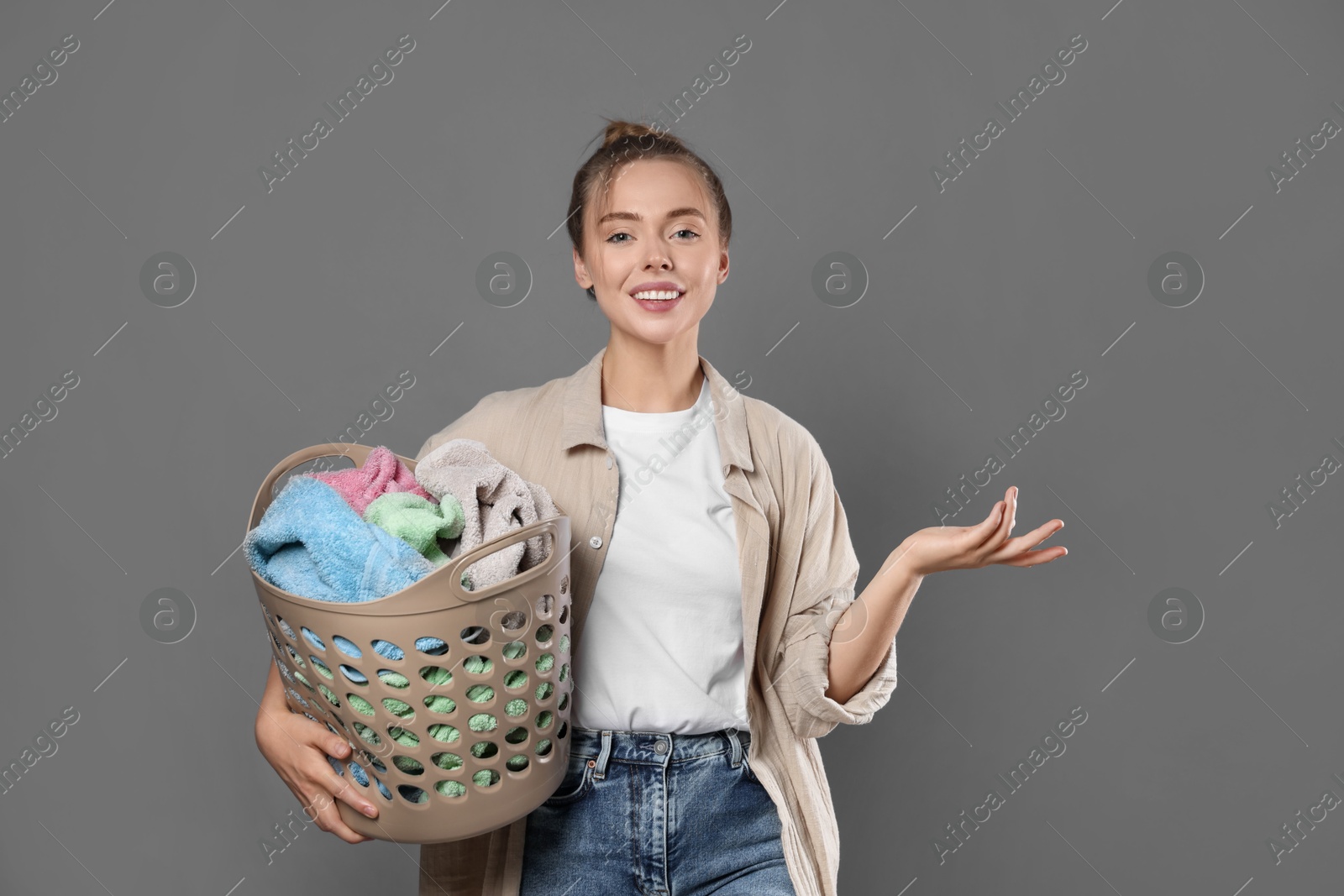 Photo of Happy young housewife with basket full of laundry on grey background