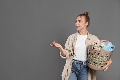 Happy young housewife with basket full of laundry on grey background. Space for text