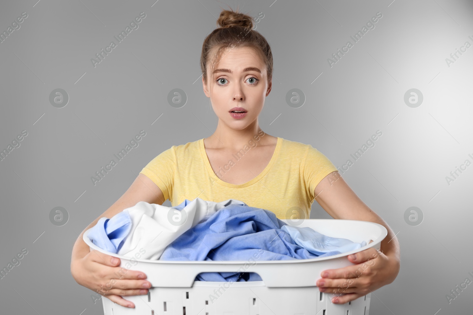 Photo of Tired housewife with basket full of laundry on grey background