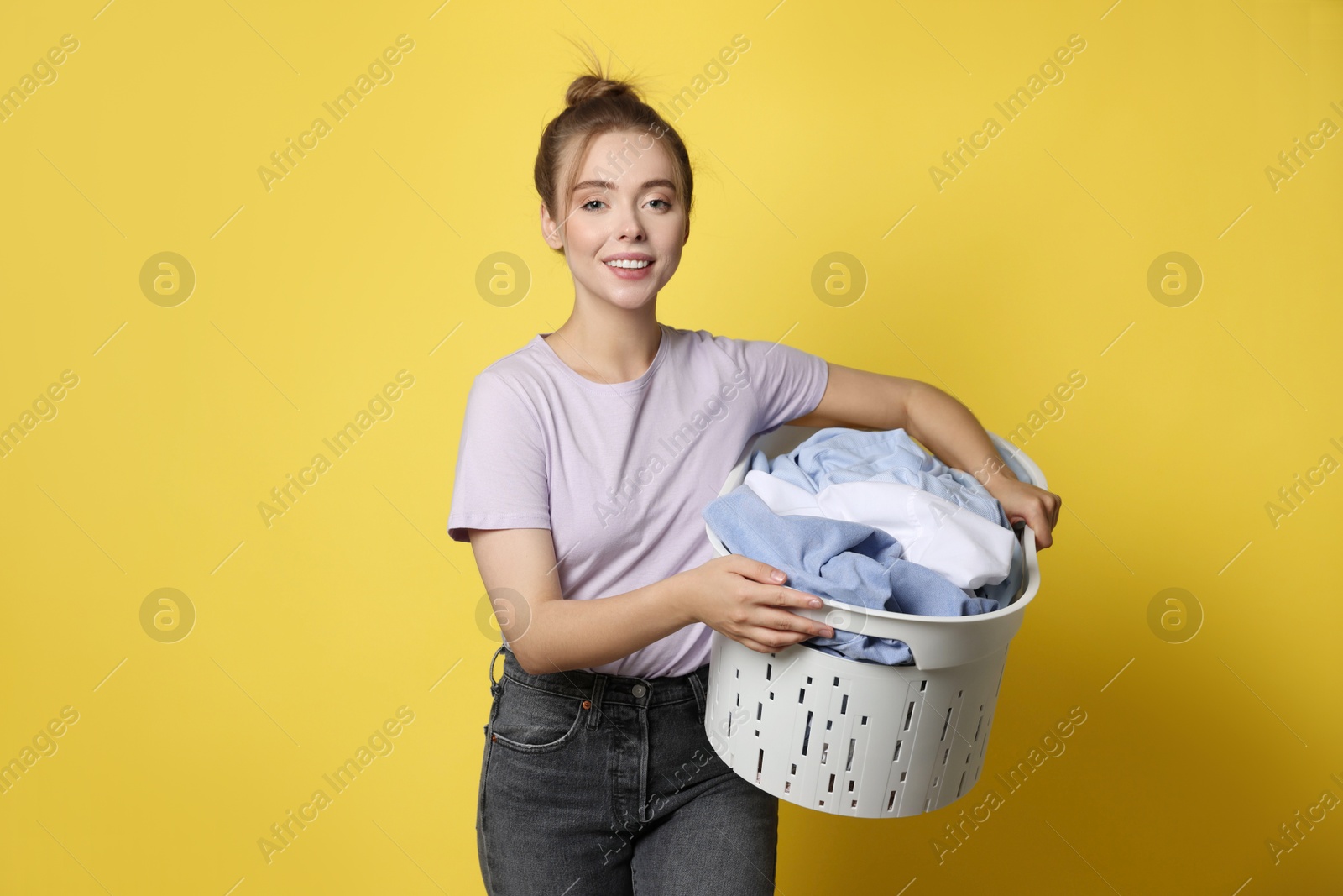 Photo of Happy young housewife with basket full of laundry on yellow background