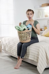 Photo of Emotional housewife with basket full of laundry on bed at home