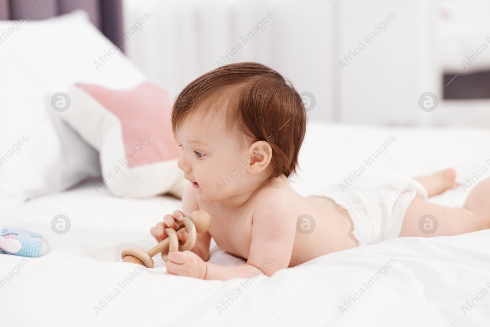 Photo of Cute little girl in diaper with wooden teether on bed at home