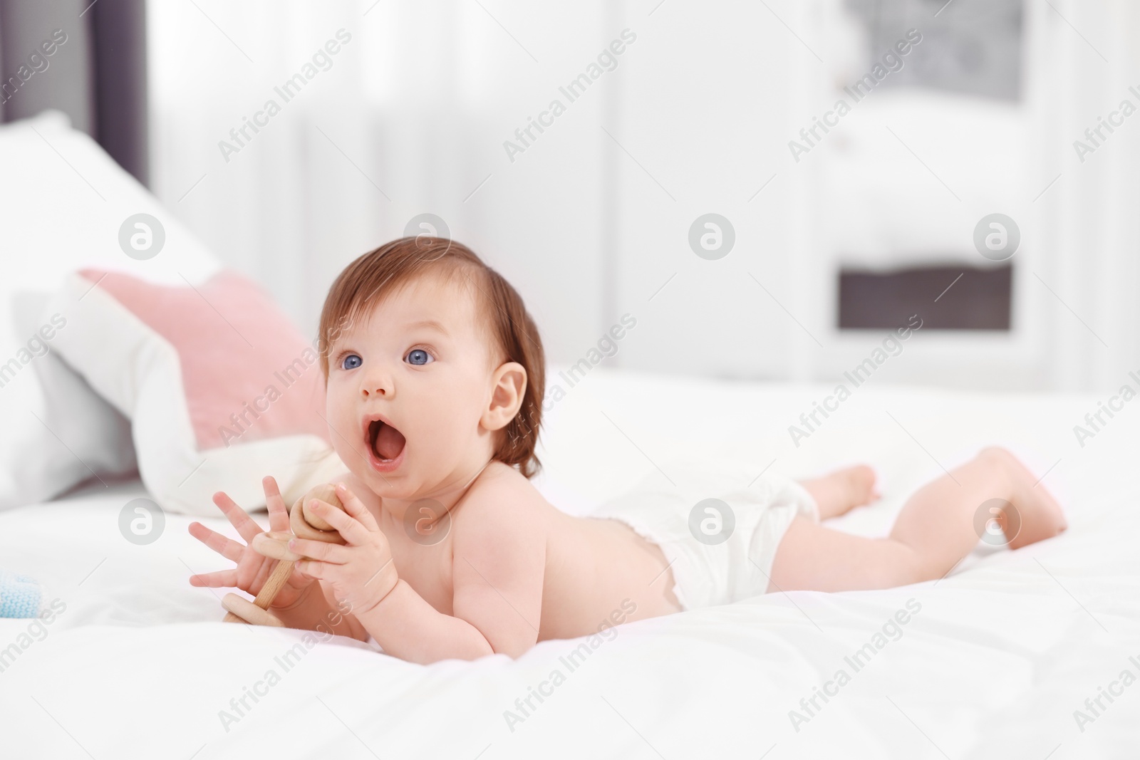 Photo of Cute little girl in diaper with wooden teether on bed at home