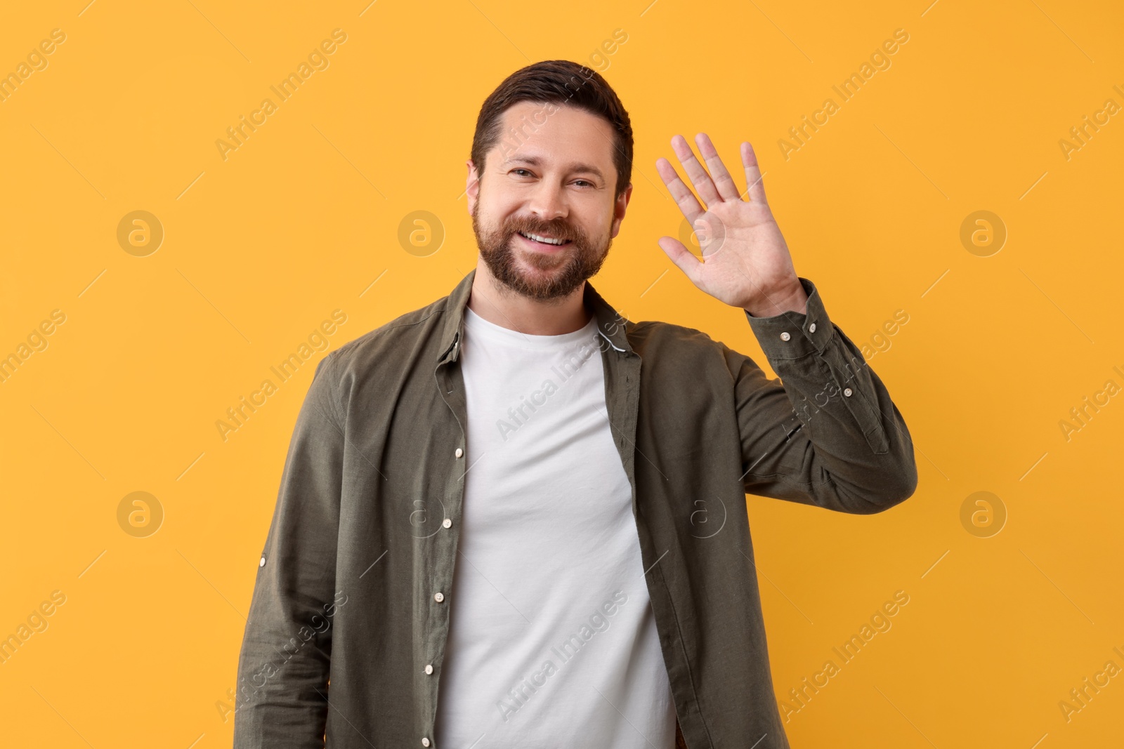 Photo of Cheerful handsome man waving on orange background