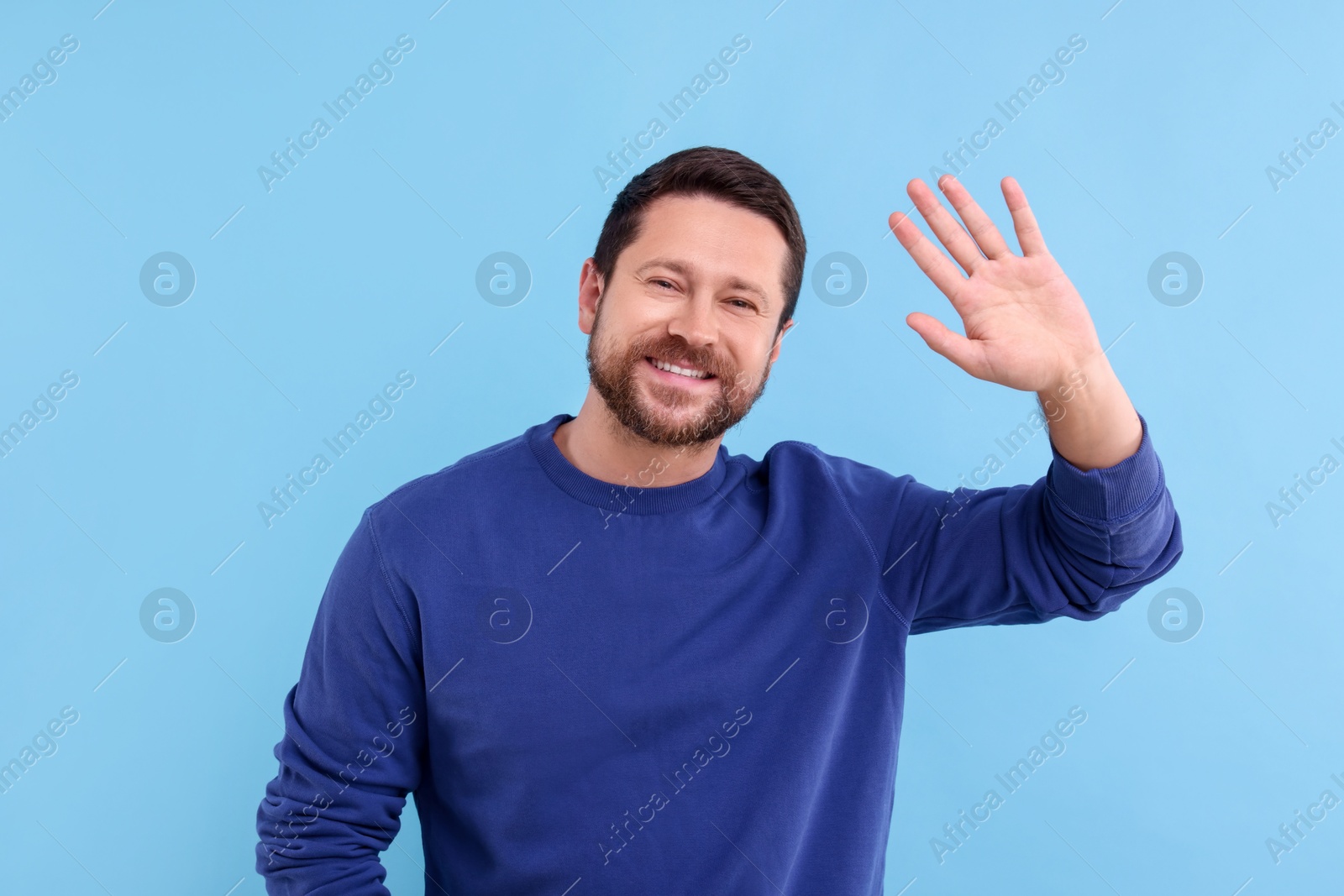 Photo of Cheerful man waving on light blue background