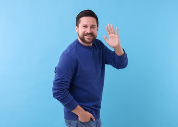 Cheerful man waving on light blue background