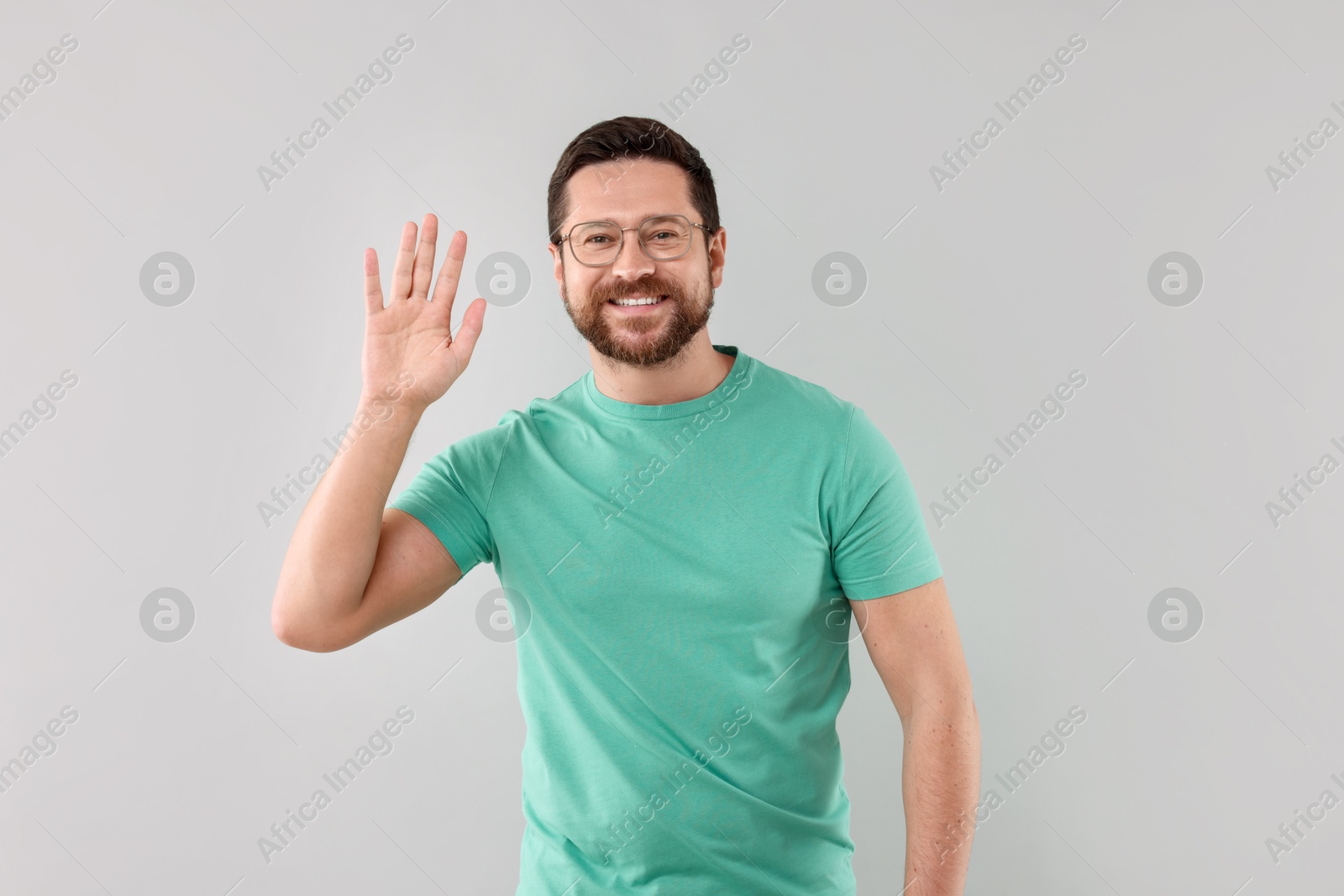 Photo of Cheerful handsome man waving on light background