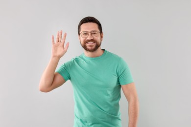 Photo of Cheerful handsome man waving on light background