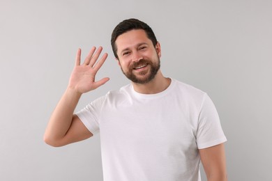 Cheerful handsome man waving on light background