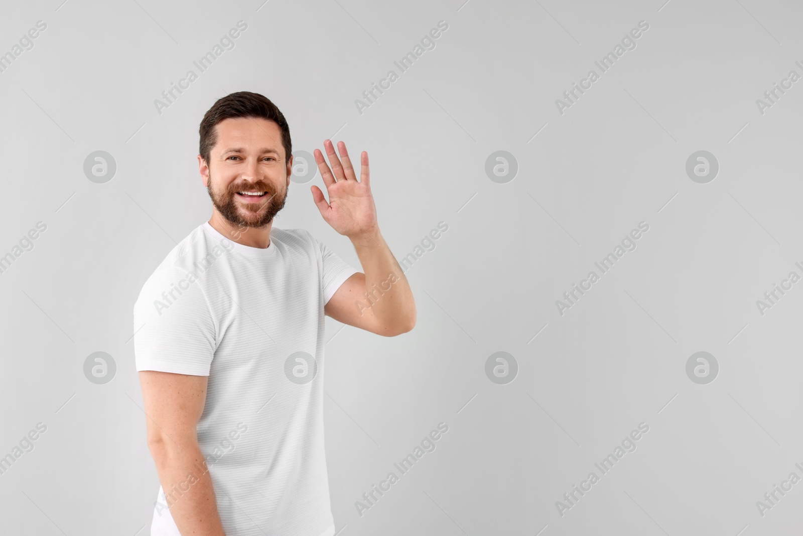 Photo of Cheerful man waving on light background. Space for text