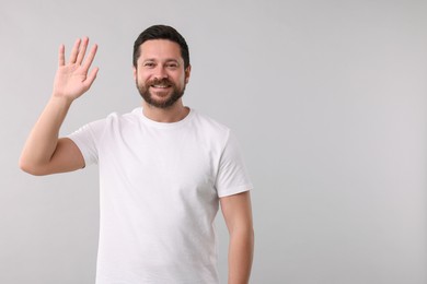 Cheerful man waving on light background. Space for text