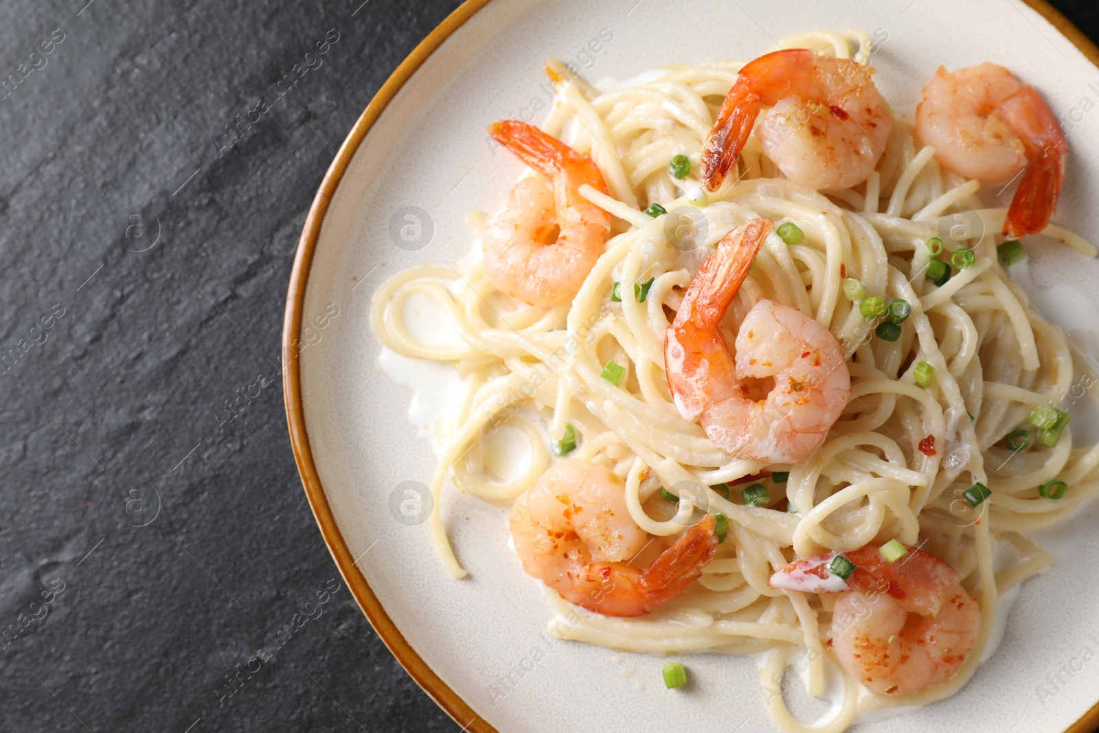 Photo of Delicious pasta with shrimps and green onion on black table, top view