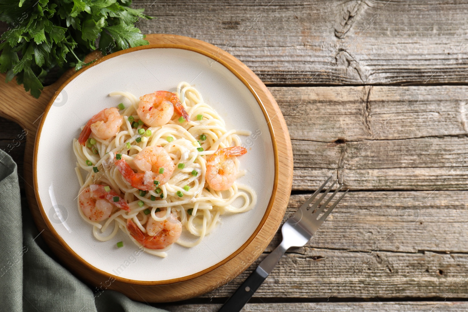 Photo of Delicious pasta with shrimps, green onions and parsley on wooden table, top view. Space for text