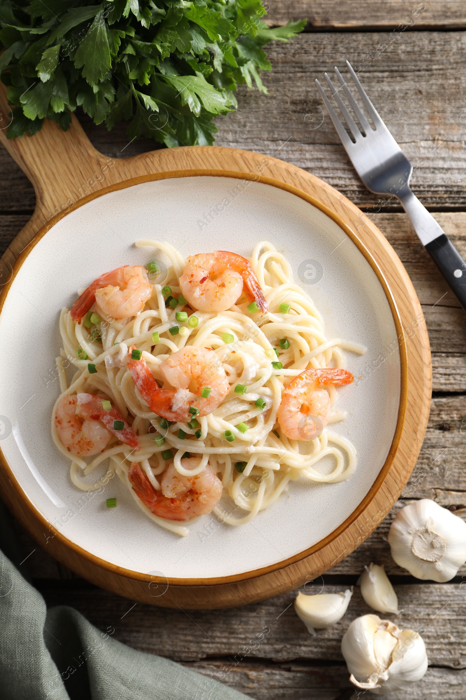 Photo of Delicious pasta with shrimps, green onions, lime, garlic and parsley on wooden table, flat lay