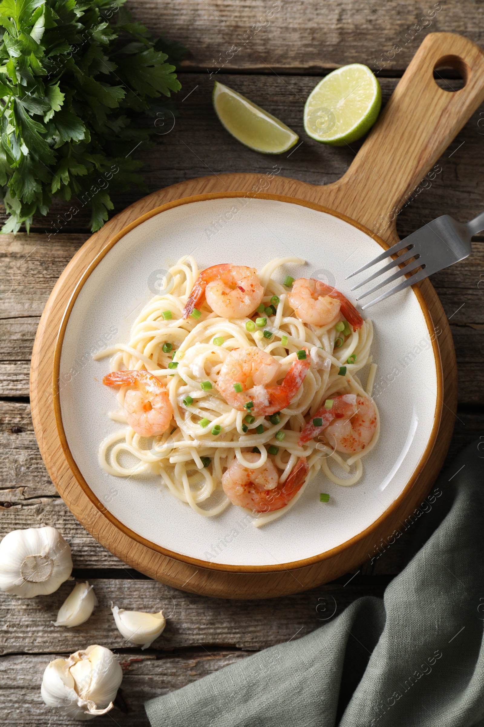 Photo of Delicious pasta with shrimps, green onions, lime, garlic and parsley on wooden table, flat lay