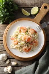 Photo of Delicious pasta with shrimps, green onions, lime, garlic and parsley on wooden table, flat lay