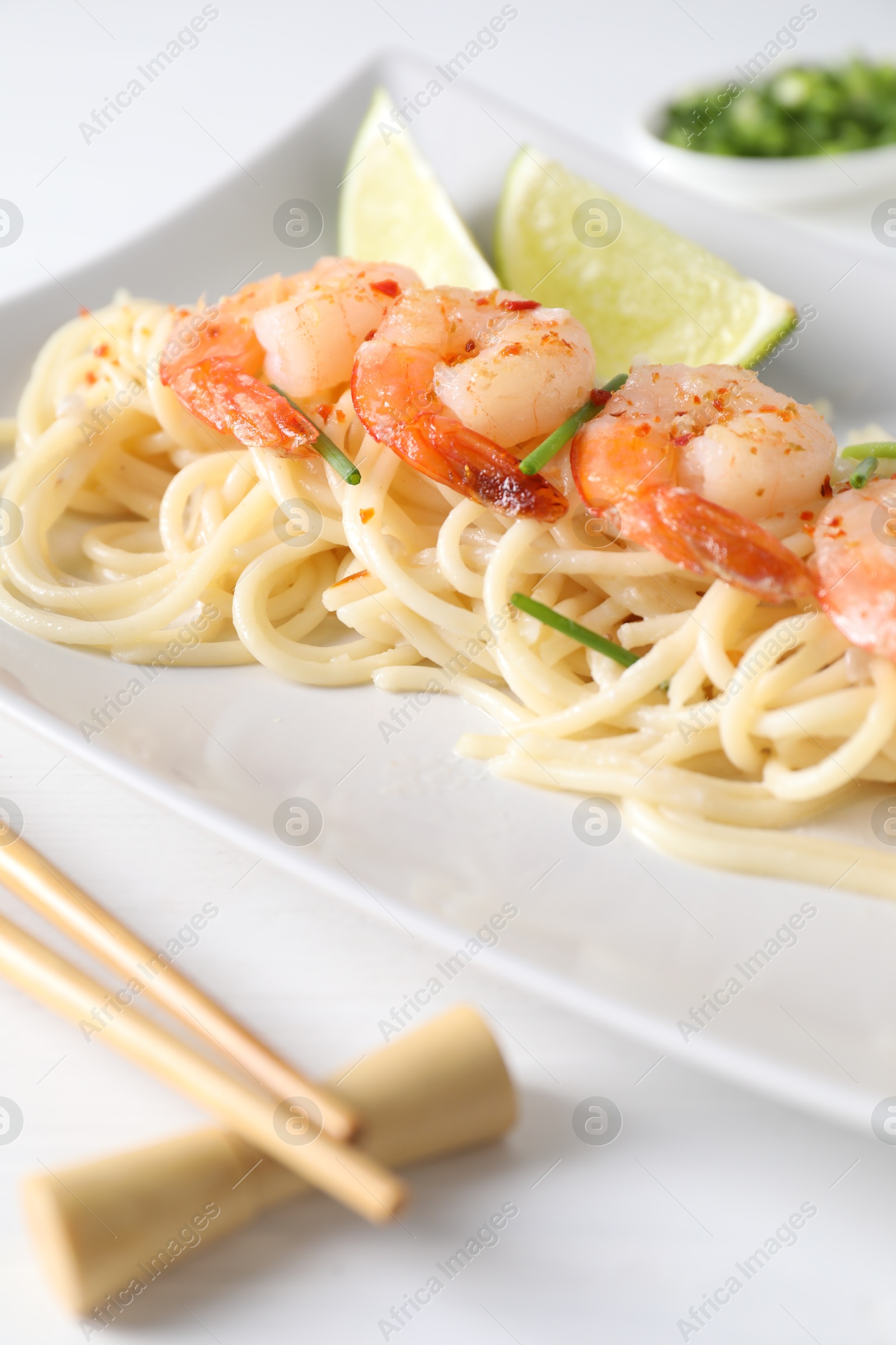 Photo of Delicious pasta with shrimps, green onions, lime and chopsticks on white table, closeup