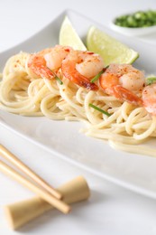 Photo of Delicious pasta with shrimps, green onions, lime and chopsticks on white table, closeup