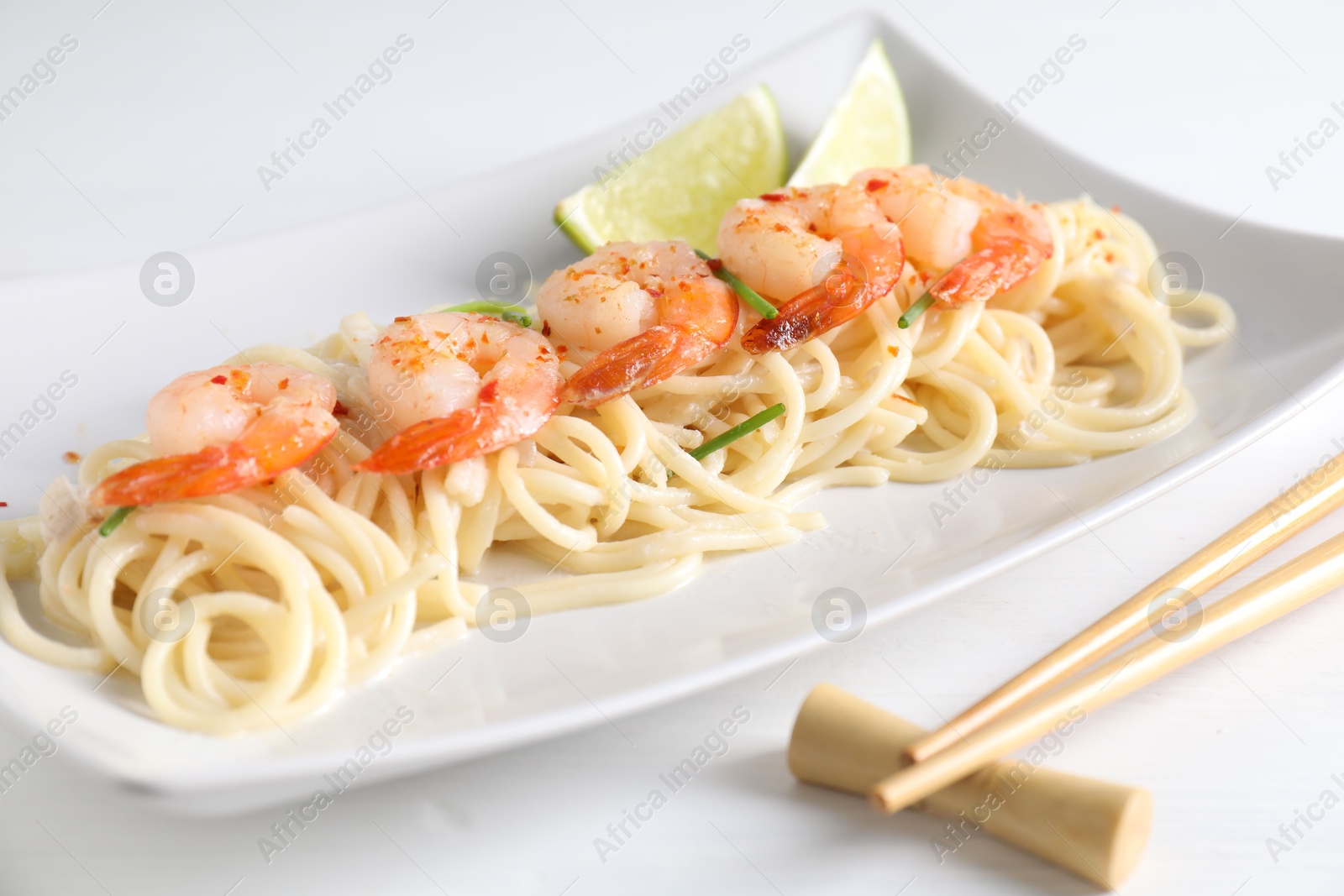 Photo of Delicious pasta with shrimps, green onions, lime and chopsticks on white table, closeup