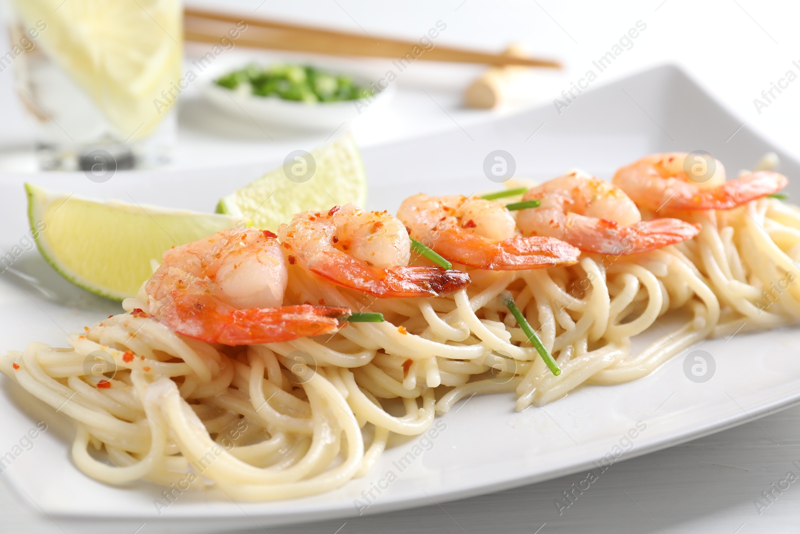 Photo of Delicious pasta with shrimps, green onions and lime on white table, closeup