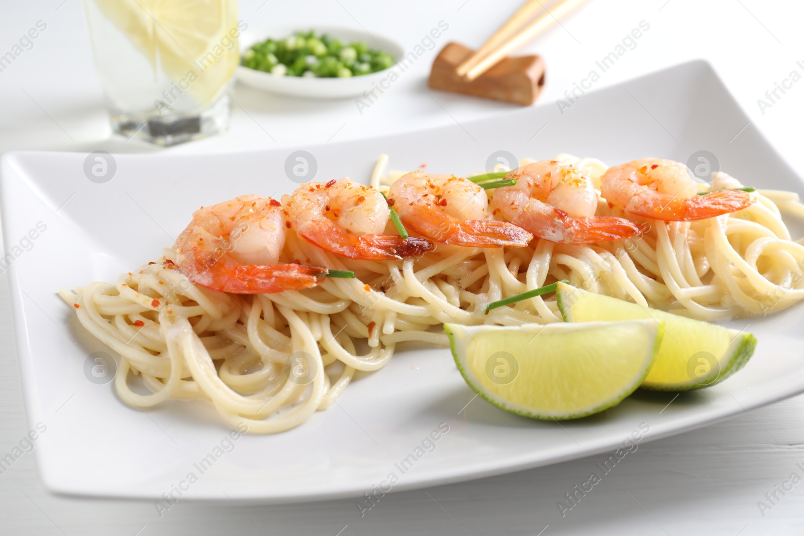 Photo of Delicious pasta with shrimps, green onions and lime on white table, closeup