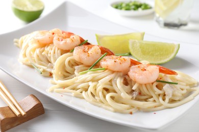 Photo of Delicious pasta with shrimps, green onions, lime and chopsticks on white wooden table, closeup