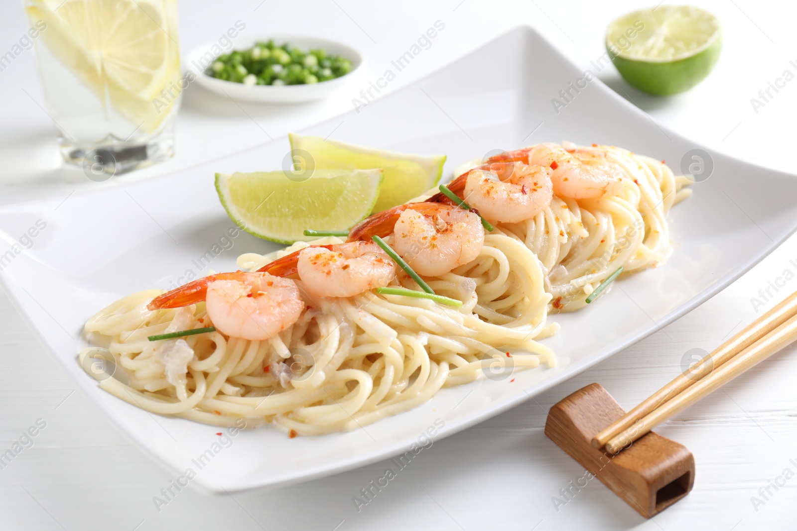 Photo of Delicious pasta with shrimps, green onions, lime and chopsticks on white wooden table, closeup