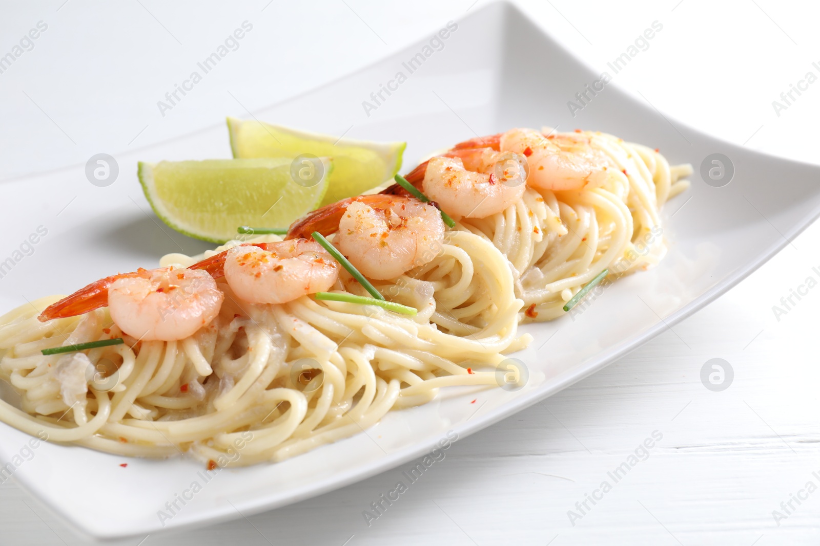 Photo of Delicious pasta with shrimps, green onions and lime on white wooden table, closeup