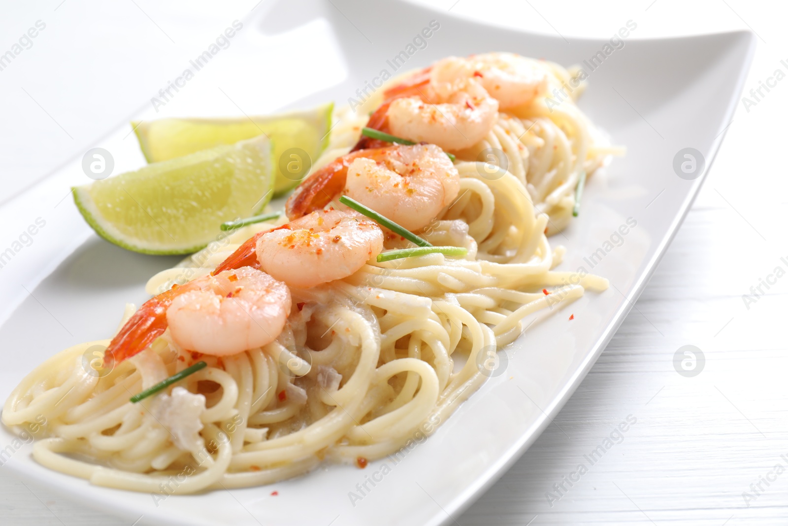 Photo of Delicious pasta with shrimps, green onions and lime on white wooden table, closeup