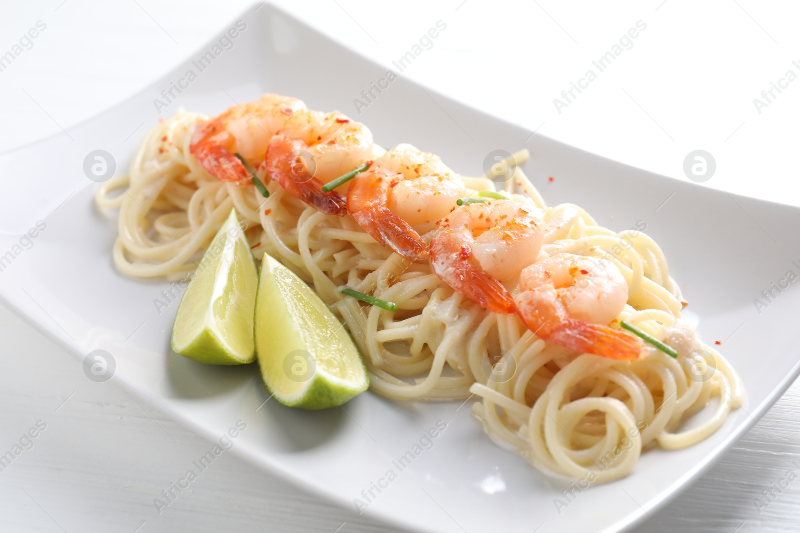 Photo of Delicious pasta with shrimps, green onions and lime on white wooden table, closeup