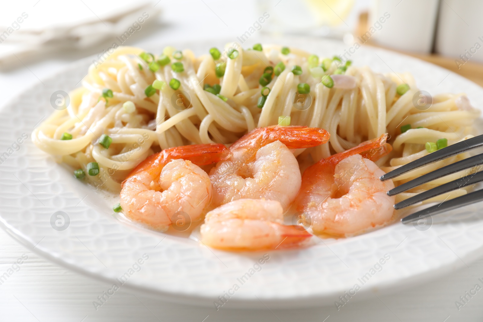 Photo of Delicious pasta with shrimps and green onions on white table, closeup