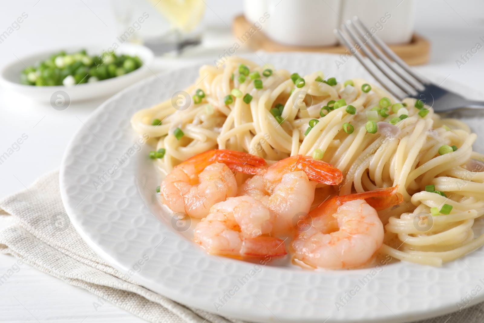 Photo of Delicious pasta with shrimps and green onions on white table, closeup