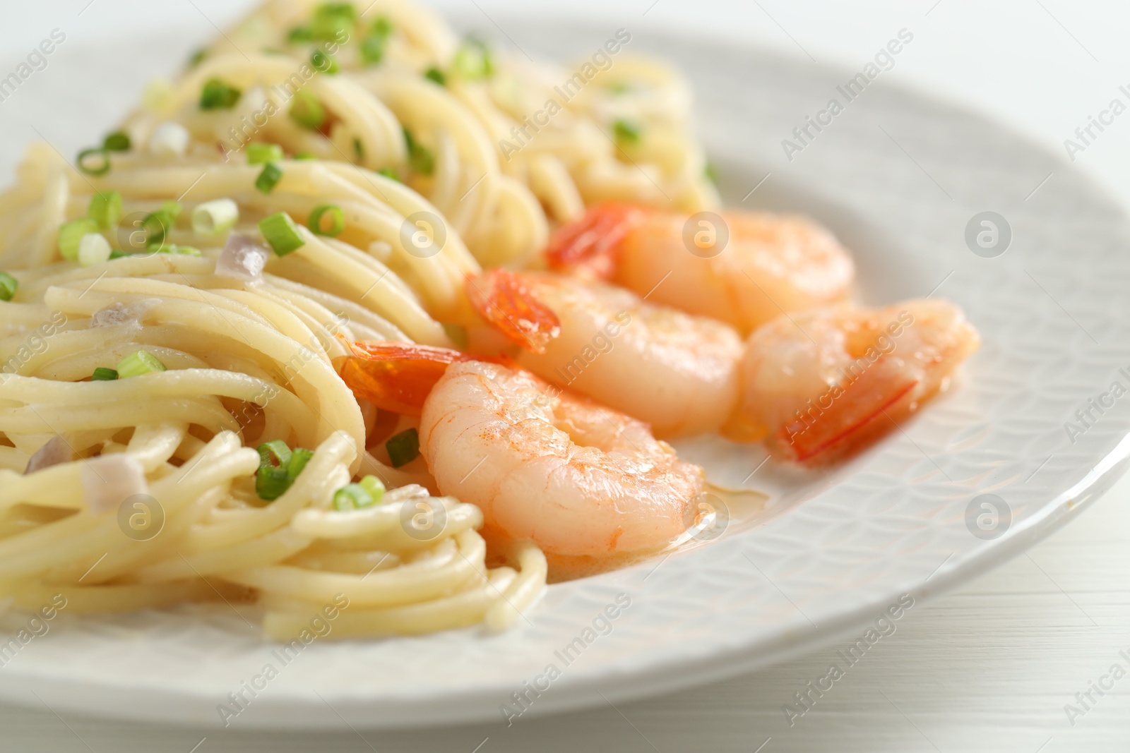 Photo of Delicious pasta with shrimps and green onions on white wooden table, closeup