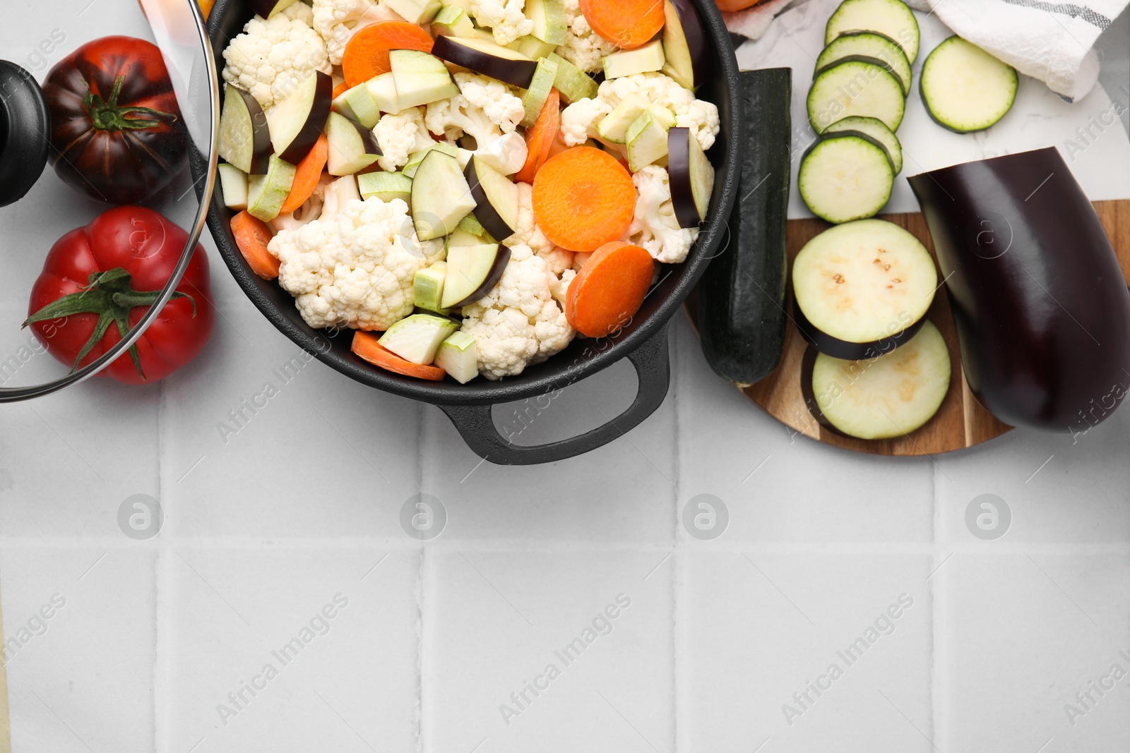 Photo of Cooking stew. Cut raw vegetables in pot on white tiled table, flat lay