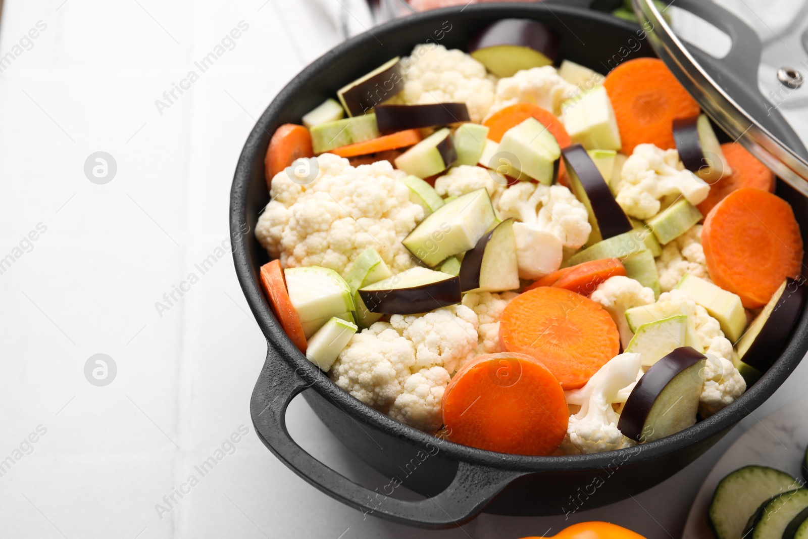 Photo of Cooking stew. Cut raw vegetables in pot on white tiled table, closeup