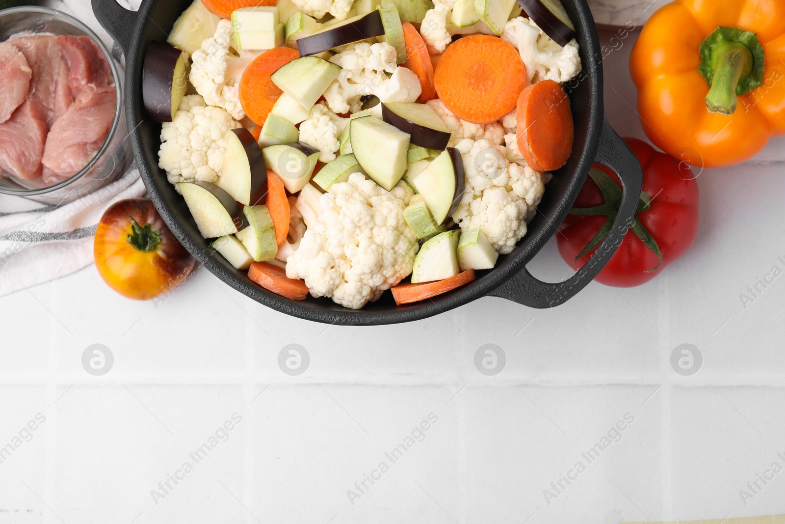 Photo of Cooking stew. Cut raw vegetables in pot and other ingredients on white tiled table, flat lay