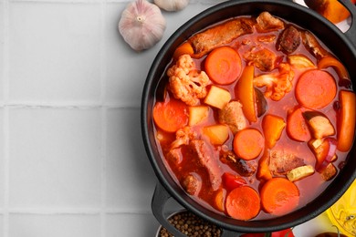 Photo of Tasty homemade stew with vegetables on white tiled table, flat lay. Space for text