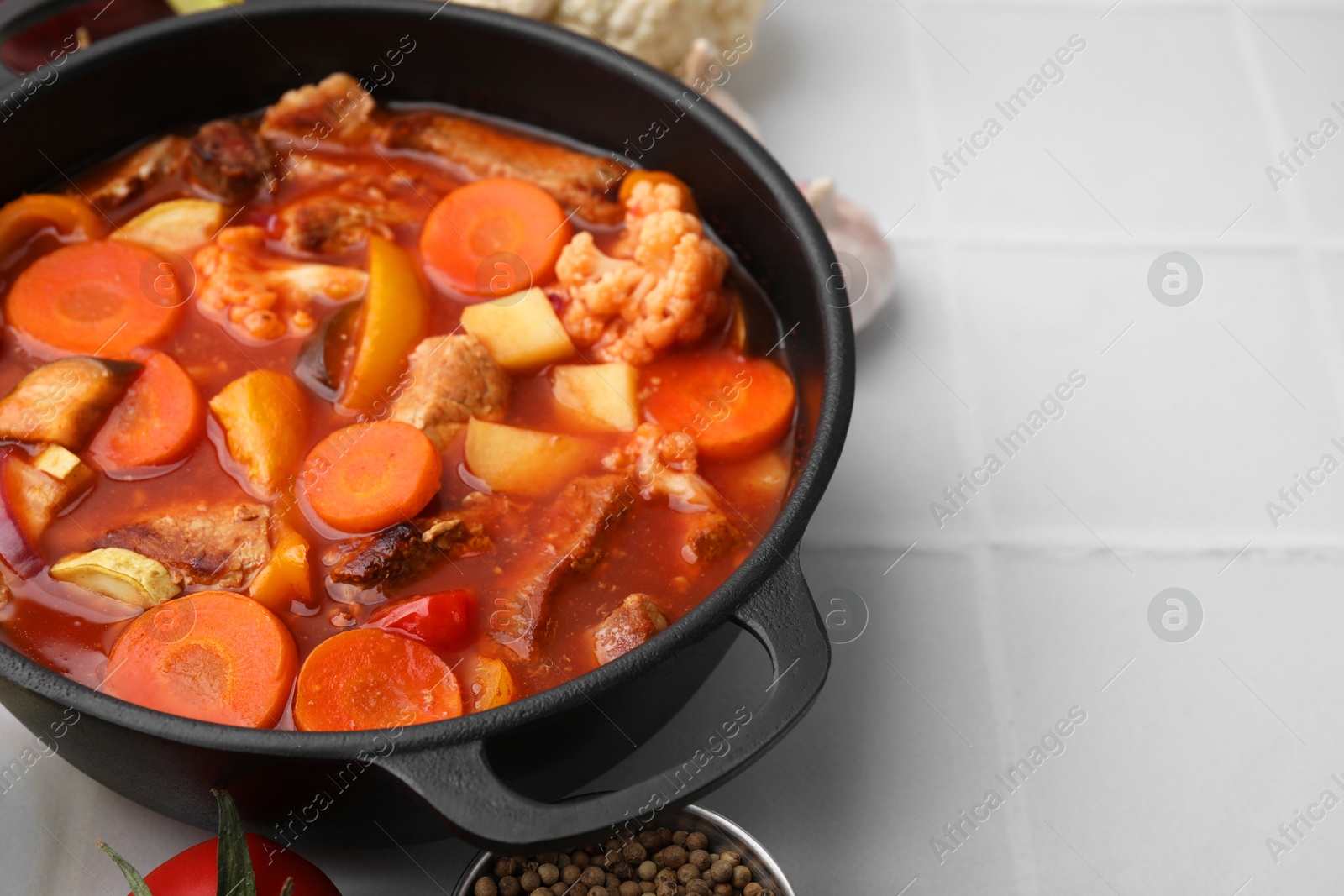 Photo of Tasty homemade stew with vegetables on white tiled table, closeup. Space for text