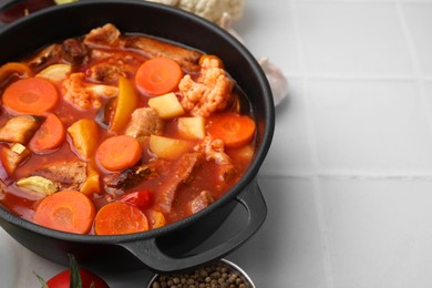 Tasty homemade stew with vegetables on white tiled table, closeup. Space for text