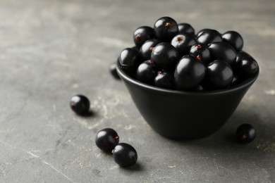 Photo of Ripe black currants in bowl on grey table. Space for text