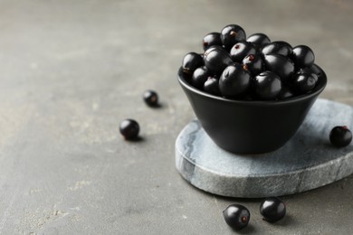 Ripe black currants in bowl on grey table. Space for text