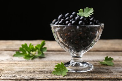 Ripe black currants and leaves in glass dessert bowl on wooden table, space for text