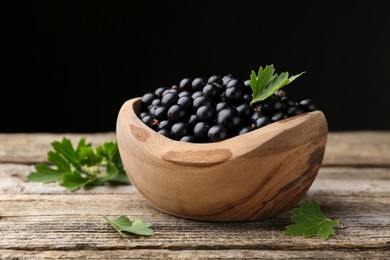 Photo of Ripe black currants and leaves in bowl on wooden table