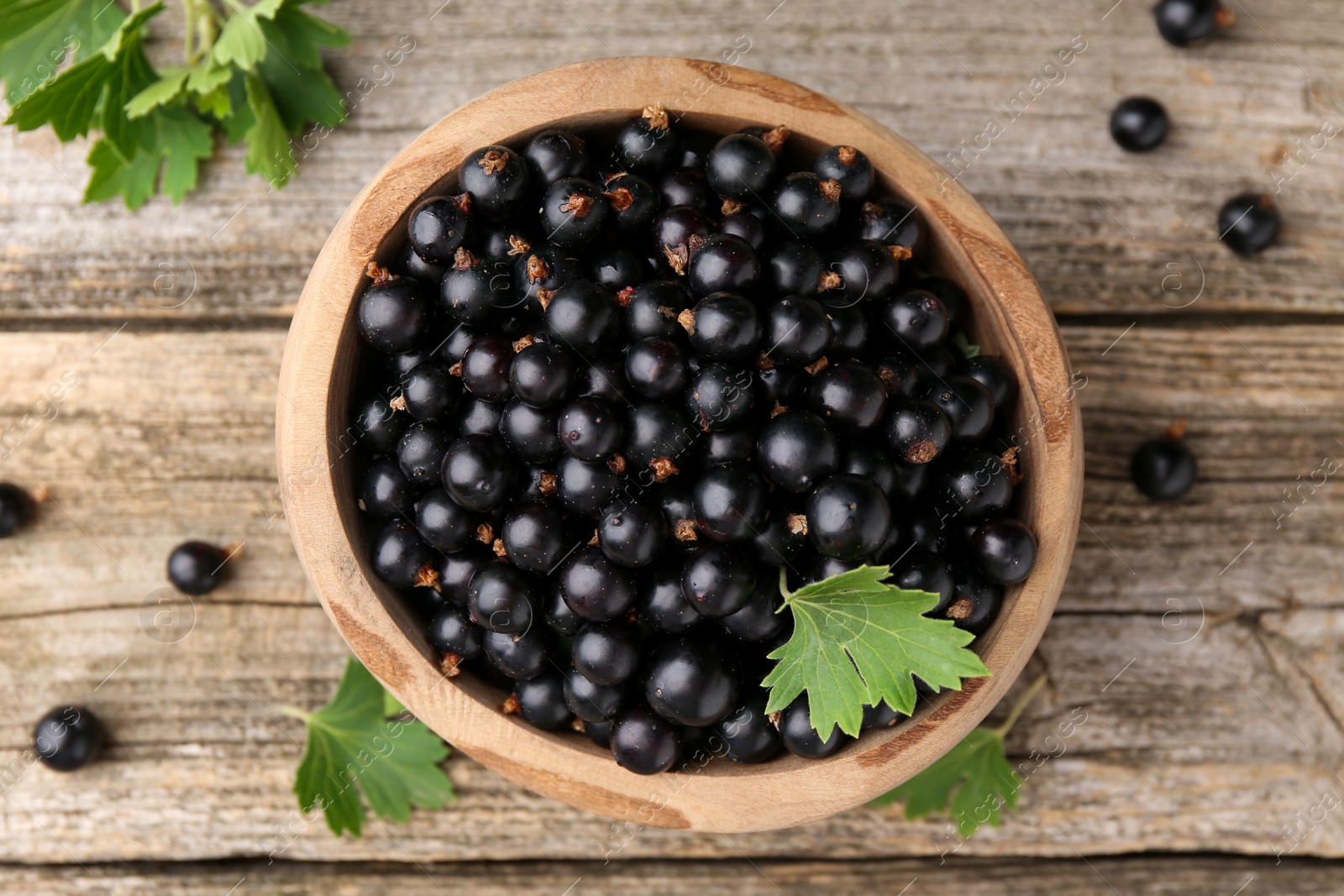 Photo of Ripe black currants and leaves in bowl on wooden table, top view